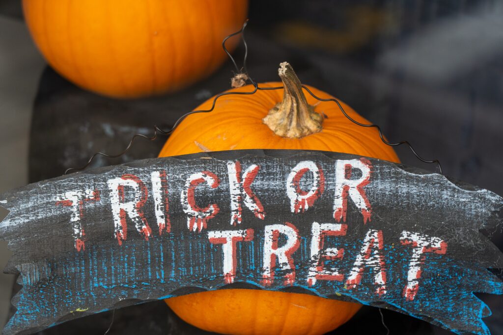 A wooden sign which reads Trick or Treat. Behind the sign is two pumpkins.